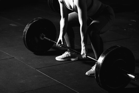 Young strong muscular fit girl with big muscles preparing for hard strength weight lifting or dead lift cross workout training with barbell weights in the gym real people exercising