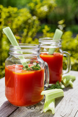 Two glasses of tomato juice with parsley and celery decorations, stand in the open air on wooden boards, the rays of the sun shine, shallow depth of field, selective focus. The concept of natural