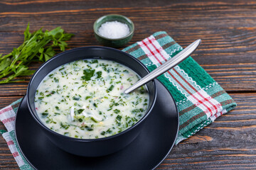 Cold soup with fresh cucumbers, radishes with yogurt in a bowl on wooden background. Traditional Russian food - okroshka. Vegetarian food. Healthy eating concept.