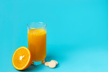 tablet of vitamins with the taste of orange is dissolved in a glass of water on a blue background.     Сoncept of natural and chemical vitamins. Copy space.