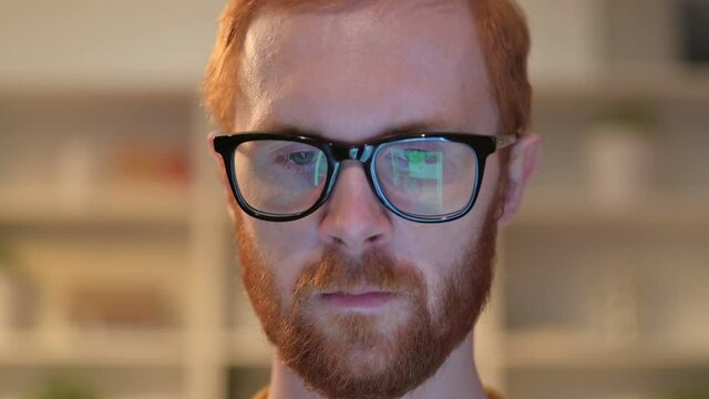 Close up of Face of Redhead Man using Device reflected on Glasses 