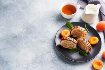 Pieces of sweet roll with cream filling on a plate. Fresh apricot berries and mint leaves.