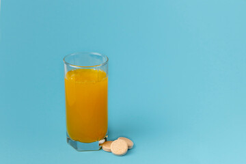 Tablet of vitamins with the taste of orange is dissolved in a glass of water on a blue background.     Сoncept of vitamins. Copy space.