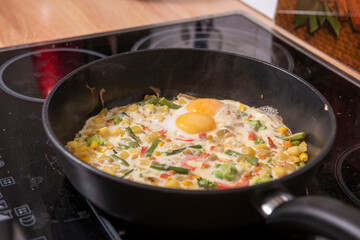 In a black pan, appetizer omelet fried eggs with fresh vegetables.