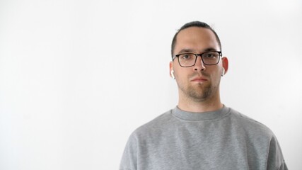 Portrait of serious attractive man in glasses and headphones. Emotional handsome guy is standing and looking at the camera on white background
