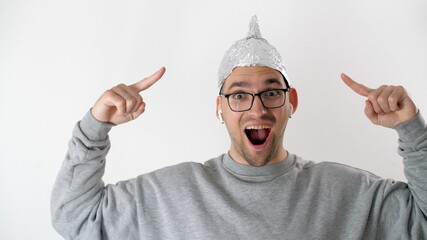 White man in a foil hat smiles and joyfully points his fingers at the tinfoil hat. 5G tower...