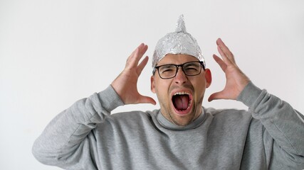 Frightened man screams that 5G radiation waves penetrate his head. Paranoid in a foil hat. White...