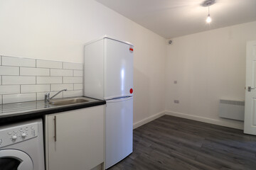 A modern British apartment kitchen and dining room with a grey wooden floor with white walls and modern fitted kitchen with washing machine, and white fridge.