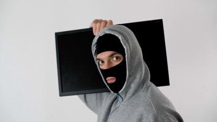 Thief in a black mask on his face steals a TV. Man carries a TV on his shoulder. Offender with a...
