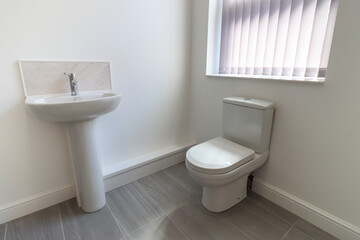 A modern British apartment living room and kitchen with black leather sofa and a coffee table on a grey wooden floor with white walls and modern fitted kitchen with a fridge