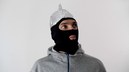 Portrait of a white frightened man in a black balaclava and a tinfoil hat  is afraid 5G waves. Thief or criminal in protective foil helmet. 5G tower radiation protection. Riots and marauding. 