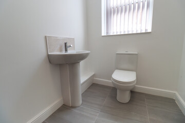 A modern British apartment living room and kitchen with black leather sofa and a coffee table on a grey wooden floor with white walls and modern fitted kitchen with a fridge