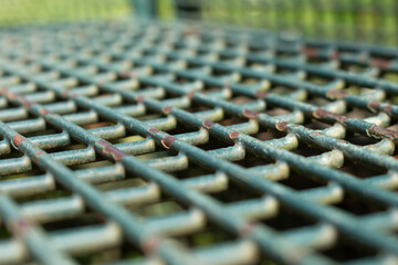 Obraz premium Slanted view of a green metal park bench grid with paint peeling off, selected focus