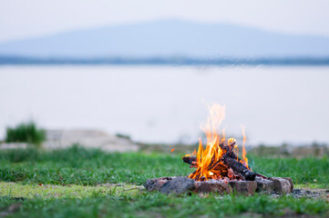 Small campfire with flames beside a lake with wood pile on the side.