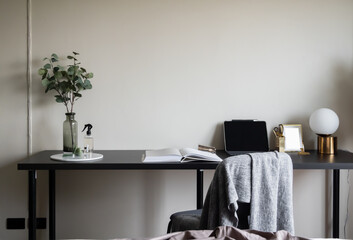 Bedroom working corner decorated with laptop, white candles and artificial plant in glass vase on black wood  working table with beige painted wall in the background /apartment interior / copy space