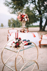 Vase with fruits, pomegranates, grapes on a glass table. Arrangement of flowers, roses, dahlia and candles. Banquet on the nature, sand, trees