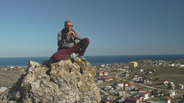 A man sits on a stone against the background of the sea and the valley with the city and plays the pipe The idea of carelessness and tranquility