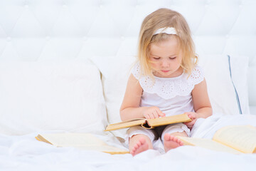 A small child reads a book leading a finger through the pages of a textbook