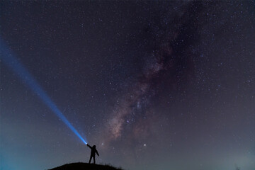 Silhouette of a man with a flashlight, observing beautiful, wide blue night sky with stars and...