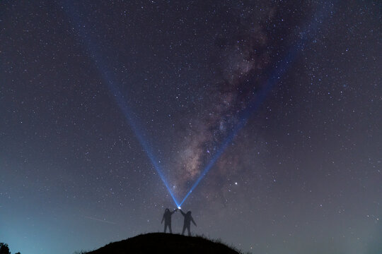 Silhouette of a man with a flashlight, observing beautiful, wide blue night sky with stars and Milky way galaxy. Astronomy, orientation, clear sky concept and background.