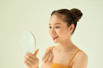 Beautiful young Asian woman applying lipstick over light background.