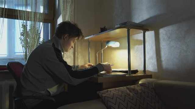 Student businessman working in a dark room with a desk lamp with documents. The student solves homework in his room in the evening.