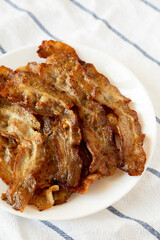 Homemade Fried Bacon on a white plate, side view. Close-up.