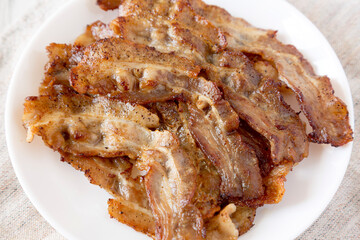 Homemade Fried Bacon on a white plate on a white wooden background, low angle view. Close-up.