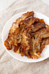Homemade Fried Bacon on a white plate on a white wooden background, side view. Close-up.