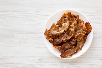 Homemade Fried Bacon on a white plate on a white wooden background, top view. Overhead, from above, flat lay. Copy space.