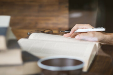 Right hand writing on a book in library with eyeglasses.
