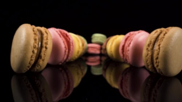 Macro view moving past colorful macarons on black glass and black background, french pastry dessert