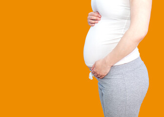 Pregnant woman in a white t-shirt and gray pants on a background of an orange wall