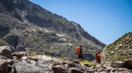 Mountaineers walking with backpacks in the mountains on a sunny summer day under a clear blue sky