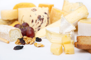 Various cheeses and snacks, bunch of grapes, raisin, walnuts, toasted bread. Closeup shot, isolated objects on white background. Gourmet or rustic food concept