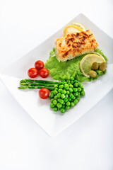 Cod fillet baked with cheese and onions with a garnish from an asparagus and green peas. On white background. High key. Selective focus.