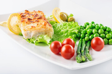 Fototapeta na wymiar Cod fillet baked with cheese and onions with a garnish from an asparagus and green peas. On white background. High key. Selective focus.
