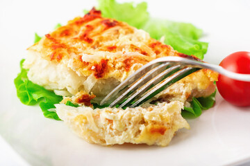 Cod fillet baked with cheese and onions with a garnish from an asparagus and green peas. On white background. High key. Selective focus. Close up.