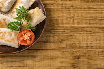 Hot pita bread wrapped with cheese and vegetables and greens on a rustic plate.