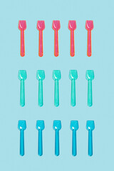 Cucharas de plástico de colores para helados sobre un fondo liso celeste. Vista superior y de cerca.