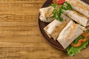 Hot pita bread wrapped with cheese and vegetables and greens on a rustic plate.
