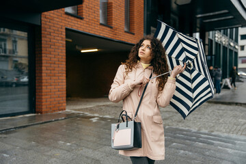 Obraz premium Сharming young curly mestizo woman under umbrella walking the street of megapolis city in rainy day