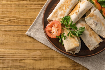 Hot pita bread wrapped with cheese and vegetables and greens on a rustic plate.