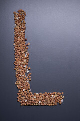Letter 'L' written with buckwheat On gray background, top view, copy space. Food supplies crisis, food donation on quarantine isolation period