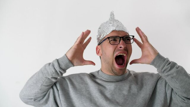 Man in a foil hat in horror screams loudly and holds his hands behind his head. Protective tinfoil helmet to the brain. 5G tower radiation protection. Irrational fear of a non-existent problem. 