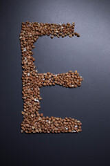 Letter 'E' written with buckwheat On gray background, top view, copy space. Food supplies crisis, food donation on quarantine isolation period
