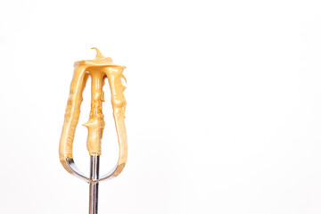 Close-up of coffee cream on metal whisk on light background for dalgona coffee. Copy space. Culinary whisk with brown cream.