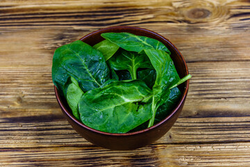 Ceramic bowl with spinach leaves on rustic wooden table