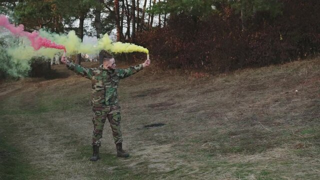 Brave fighter raises and plays with pink and yellow smoke on nature