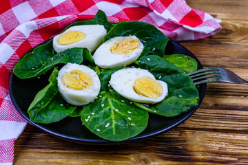 Spinach leaves and halved boiled eggs on a black plate